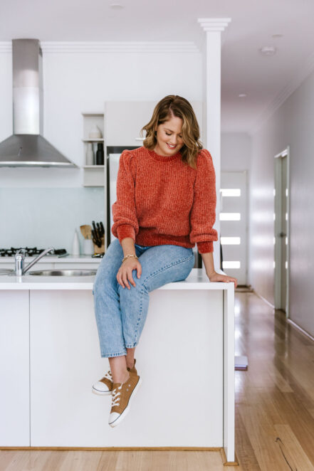 image of a girl in red sweater sitting on a kitchen bench by branding photographer Joanna Zydel